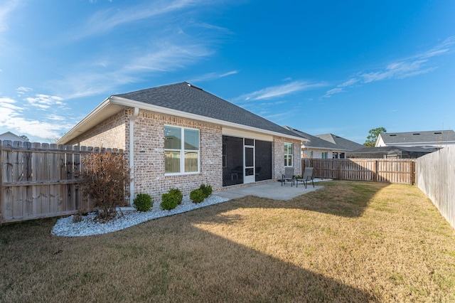 rear view of house featuring a fenced backyard, brick siding, a shingled roof, a lawn, and a patio area