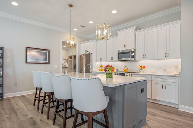 kitchen with a center island with sink, light wood finished floors, stainless steel microwave, decorative backsplash, and white cabinetry