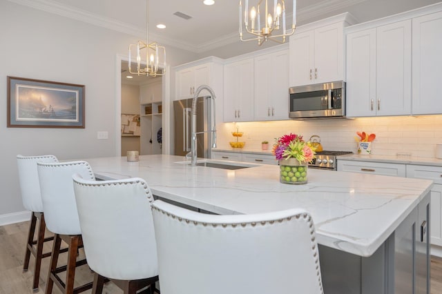 kitchen featuring a notable chandelier, stainless steel microwave, ornamental molding, backsplash, and an island with sink