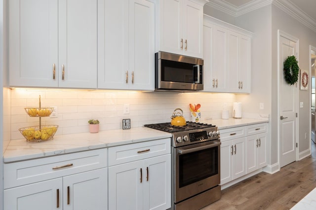 kitchen with light wood finished floors, decorative backsplash, ornamental molding, stainless steel appliances, and white cabinetry