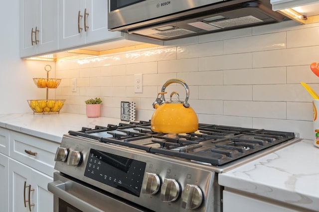 kitchen with light stone countertops, tasteful backsplash, stainless steel range with gas cooktop, and white cabinetry