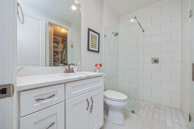 bathroom with a spacious closet, toilet, vanity, tile patterned flooring, and tiled shower