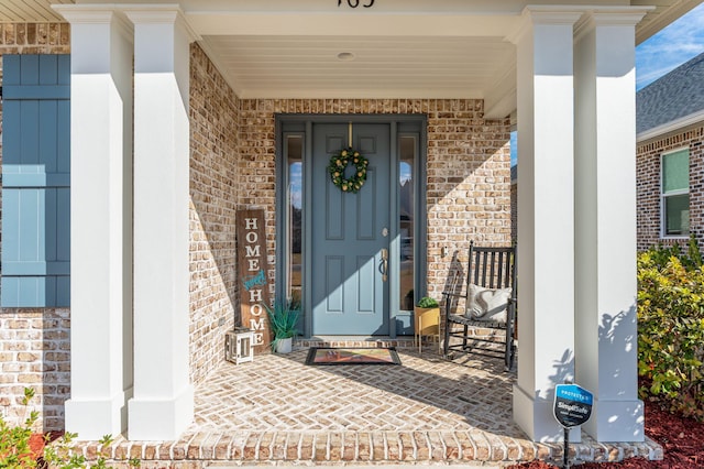 doorway to property featuring a porch and brick siding