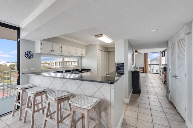 kitchen with light tile patterned floors, white cabinets, ceiling fan, ornamental molding, and a sink