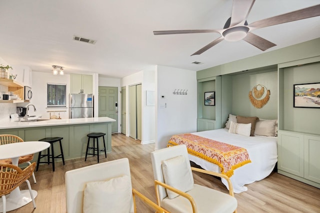 bedroom with visible vents, light wood finished floors, a sink, and freestanding refrigerator