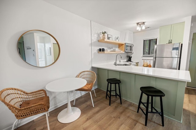 kitchen with appliances with stainless steel finishes, light wood-type flooring, light countertops, and a kitchen bar