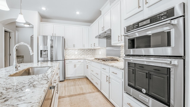 kitchen featuring under cabinet range hood, stainless steel appliances, white cabinetry, and a sink