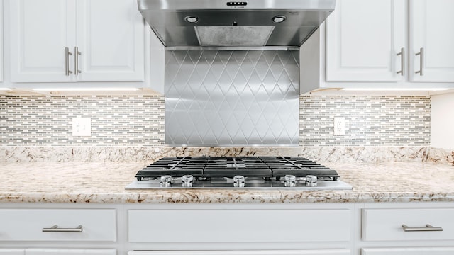 kitchen featuring wall chimney exhaust hood, stainless steel gas cooktop, white cabinets, and tasteful backsplash