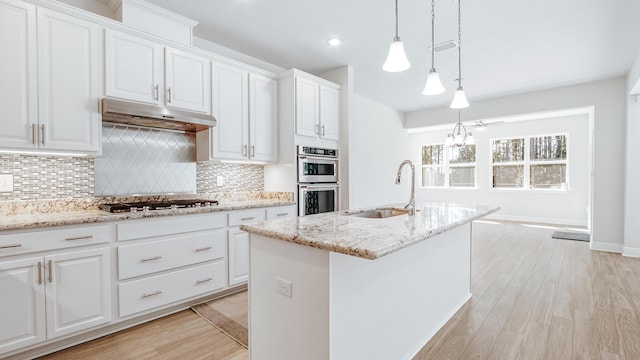 kitchen with white cabinets, a sink, backsplash, under cabinet range hood, and appliances with stainless steel finishes