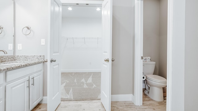 bathroom featuring wood finished floors, a walk in closet, vanity, baseboards, and toilet