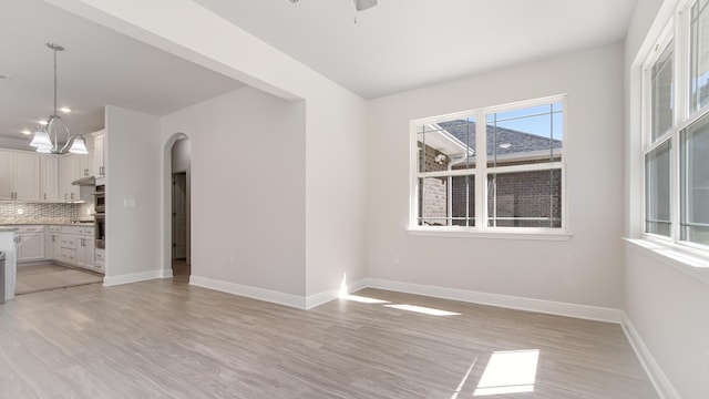 unfurnished living room with a wealth of natural light, light wood-style flooring, baseboards, and arched walkways
