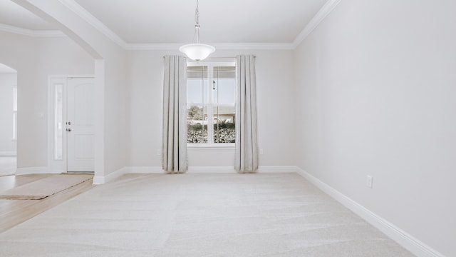 spare room featuring baseboards, arched walkways, ornamental molding, and light colored carpet