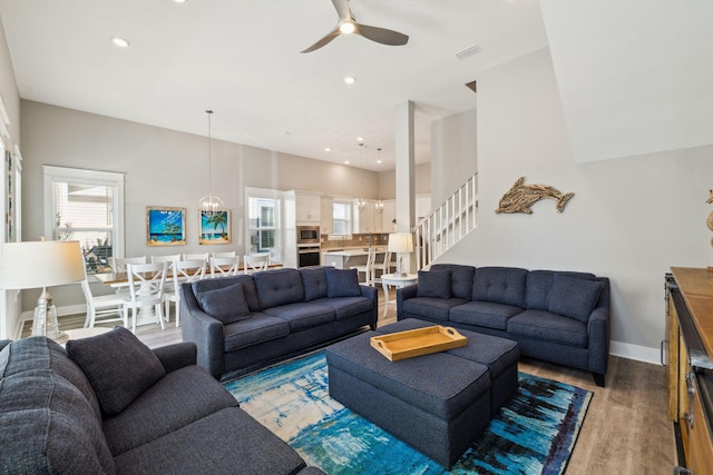 living room featuring a ceiling fan, wood finished floors, a high ceiling, baseboards, and stairs