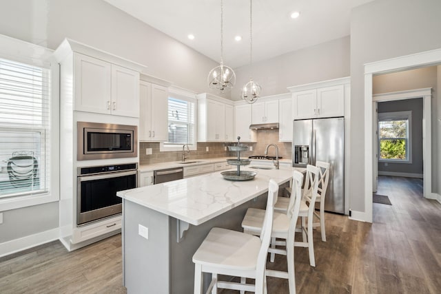 kitchen with a sink, tasteful backsplash, wood finished floors, stainless steel appliances, and white cabinets