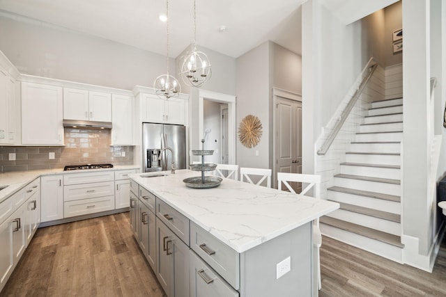 kitchen featuring a center island with sink, gray cabinets, under cabinet range hood, tasteful backsplash, and appliances with stainless steel finishes