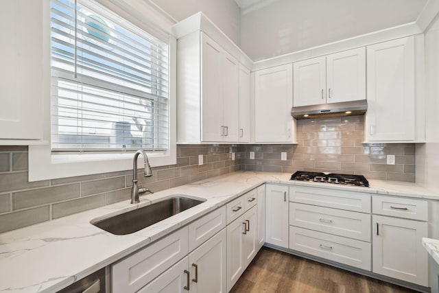 kitchen featuring a sink, under cabinet range hood, stainless steel gas stovetop, white cabinetry, and dark wood-style flooring