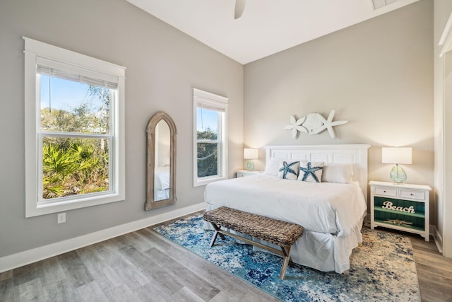 bedroom with multiple windows, a ceiling fan, baseboards, and wood finished floors