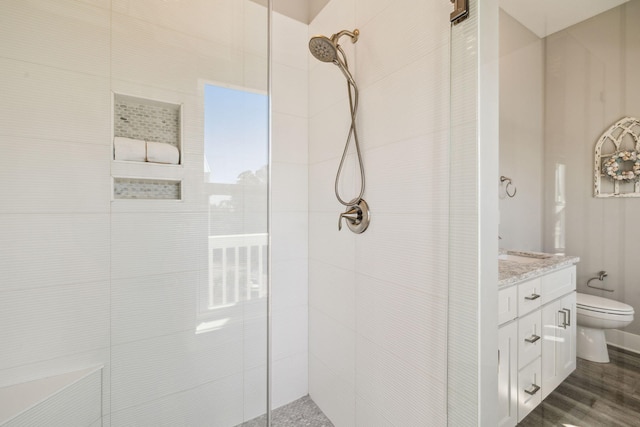 full bath with tiled shower, toilet, wood finished floors, and vanity