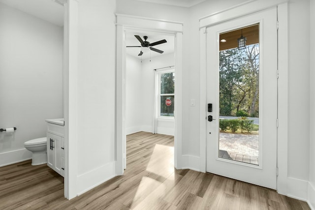 doorway featuring ceiling fan, light wood-style flooring, and baseboards