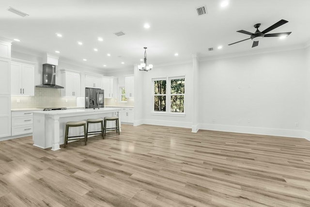 kitchen featuring decorative backsplash, stainless steel fridge with ice dispenser, open floor plan, a kitchen breakfast bar, and wall chimney range hood