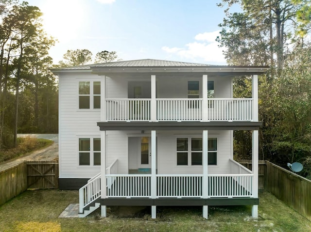 rear view of property featuring a porch, metal roof, fence, and a balcony