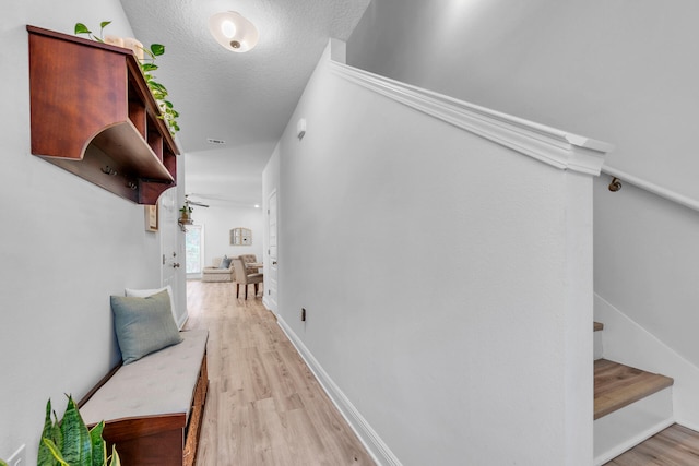 hallway with stairway, baseboards, a textured ceiling, and light wood finished floors