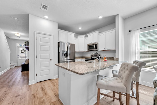 kitchen with stainless steel appliances, a peninsula, a sink, visible vents, and white cabinetry