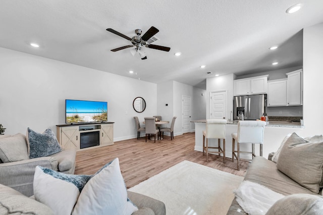 living area with ceiling fan, light wood finished floors, baseboards, and recessed lighting