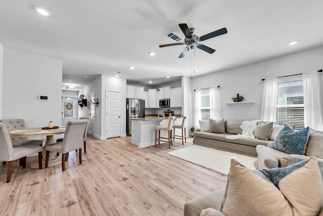 living room featuring a textured ceiling, light wood-style flooring, visible vents, and recessed lighting