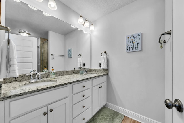 full bathroom featuring double vanity, a stall shower, a sink, a textured ceiling, and baseboards