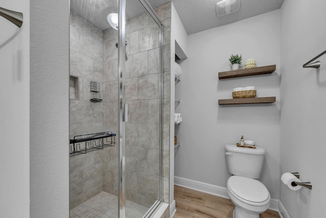 bathroom with a stall shower, wood finished floors, toilet, and baseboards