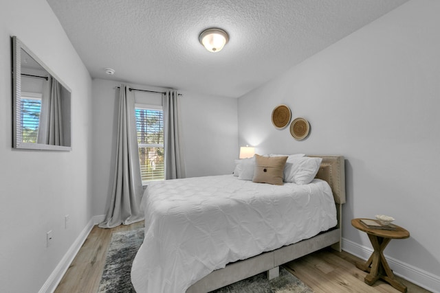 bedroom featuring a textured ceiling, baseboards, and wood finished floors