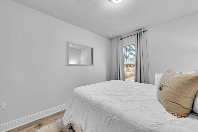 bedroom with a textured ceiling, wood finished floors, and baseboards