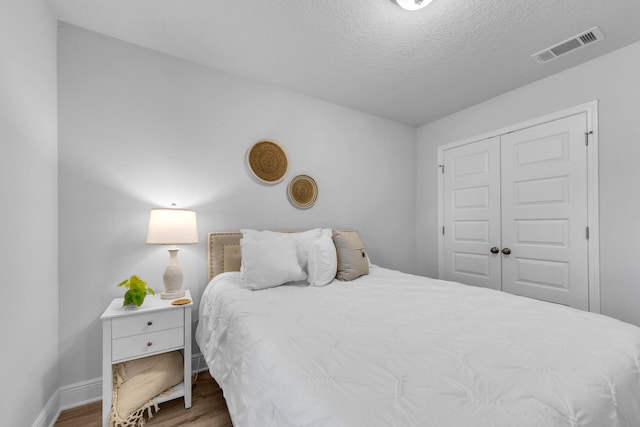 bedroom featuring a closet, visible vents, a textured ceiling, wood finished floors, and baseboards