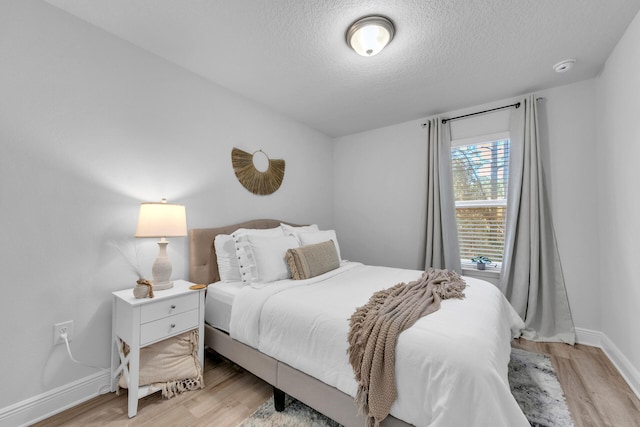 bedroom with a textured ceiling, light wood-type flooring, and baseboards