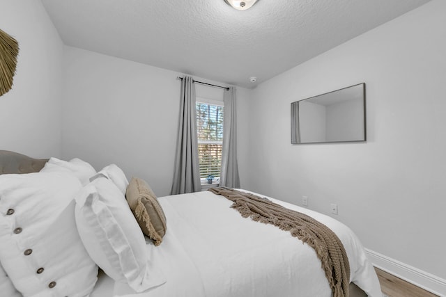 bedroom with a textured ceiling, baseboards, and wood finished floors