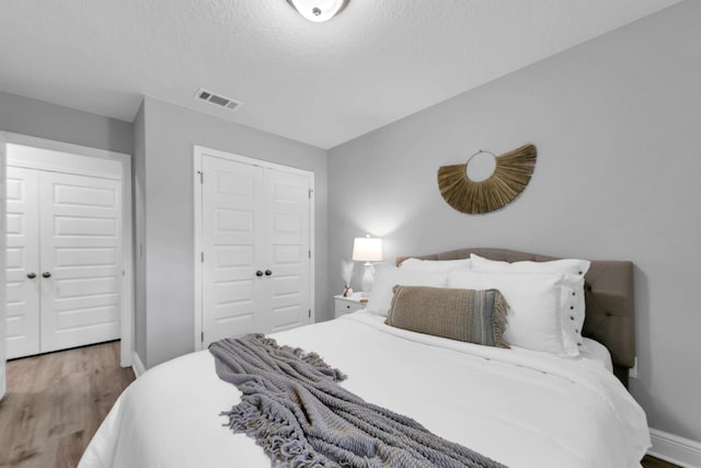 bedroom with baseboards, visible vents, wood finished floors, a textured ceiling, and a closet