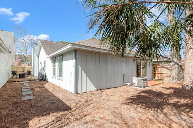 view of home's exterior featuring central AC unit, roof with shingles, fence, and a wooden deck