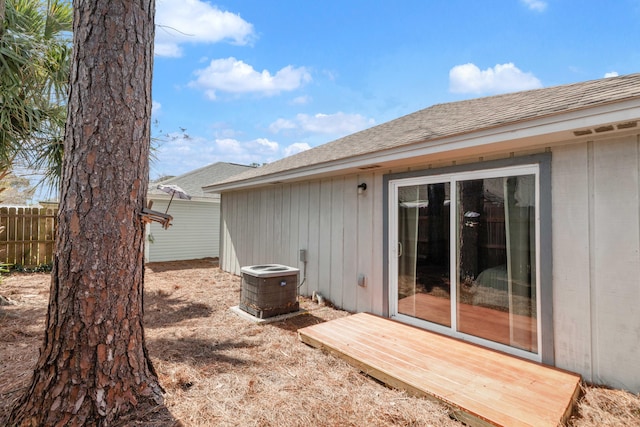 rear view of property featuring a shingled roof, fence, and central AC unit