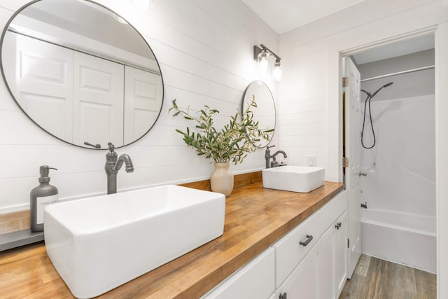 full bathroom with double vanity, shower / tub combination, a sink, and wood finished floors