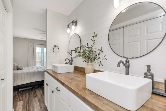 ensuite bathroom featuring double vanity, connected bathroom, a sink, and wood finished floors