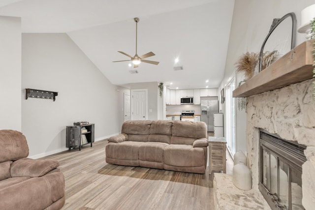 living area with baseboards, visible vents, light wood-style floors, high vaulted ceiling, and a high end fireplace