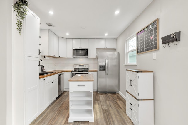 kitchen with light wood finished floors, butcher block countertops, stainless steel appliances, open shelves, and a sink