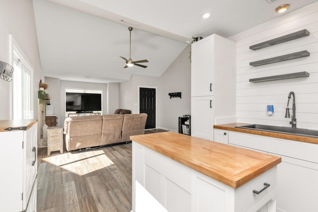 kitchen featuring white cabinets, wood counters, wood finished floors, vaulted ceiling, and a sink