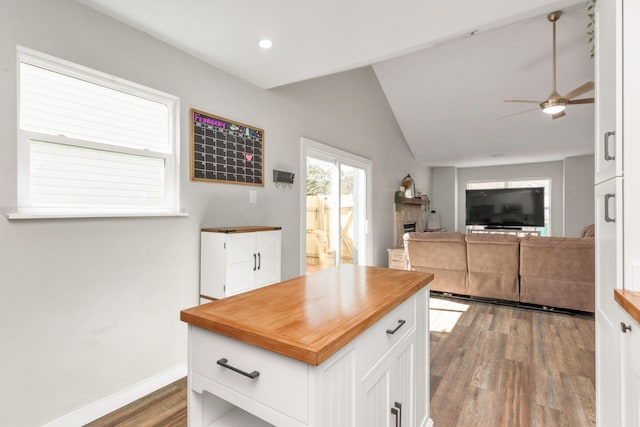 kitchen featuring white cabinets, lofted ceiling, wood counters, wood finished floors, and a fireplace