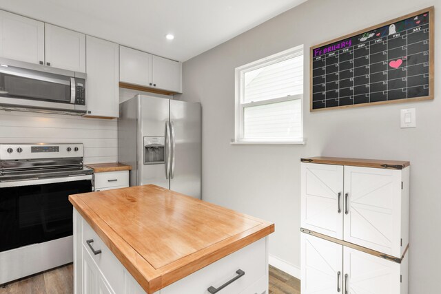 kitchen featuring stainless steel appliances, wooden counters, white cabinetry, a kitchen island, and wood finished floors