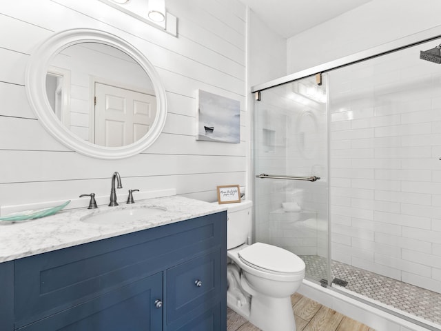 full bathroom with toilet, wooden walls, wood finished floors, vanity, and a shower stall