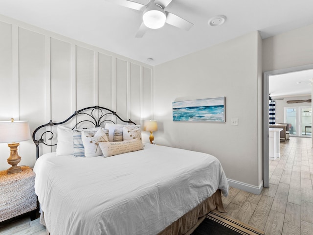 bedroom featuring a ceiling fan, a decorative wall, light wood-style flooring, and baseboards