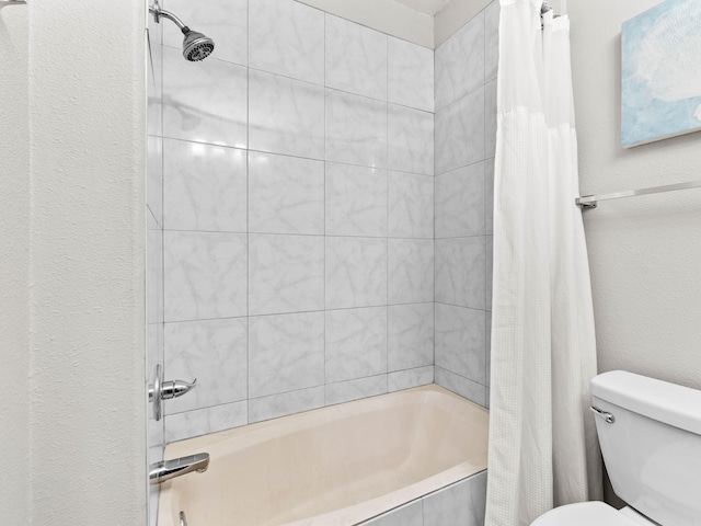 full bathroom with tiled shower / bath, a textured wall, and toilet