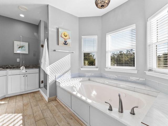 full bath featuring a jetted tub, a wealth of natural light, wood finished floors, and vanity